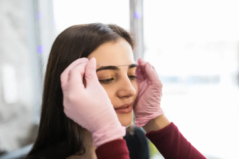 female-master-white-gloves-checks-contour-eyebrows-with-thread